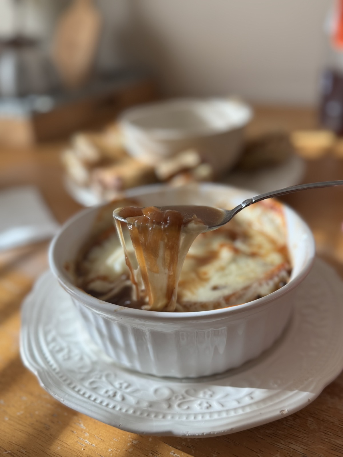 A spoon lifting melted cheese from a warm bowl of French onion soup